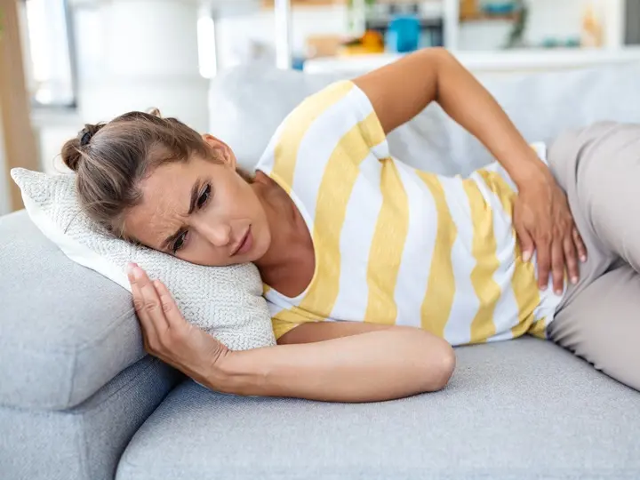 woman-lying-sofa-looking-sick-living-room-beautiful-young-woman-lying-bed-holding-hands-her-stomach-woman-having-painful-stomachache-bed-menstrual Áteresztő bél szindróma tünetei és kezelése Emésztés 
