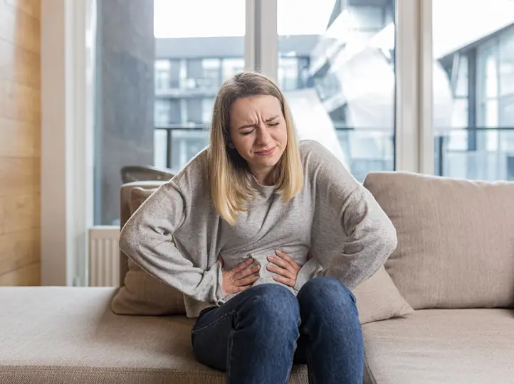 woman-sitting-sofa-holding-hands-stomach-twisted-from-pain Ételmérgezés: tünetei, megelőzés és teendők Emésztés 